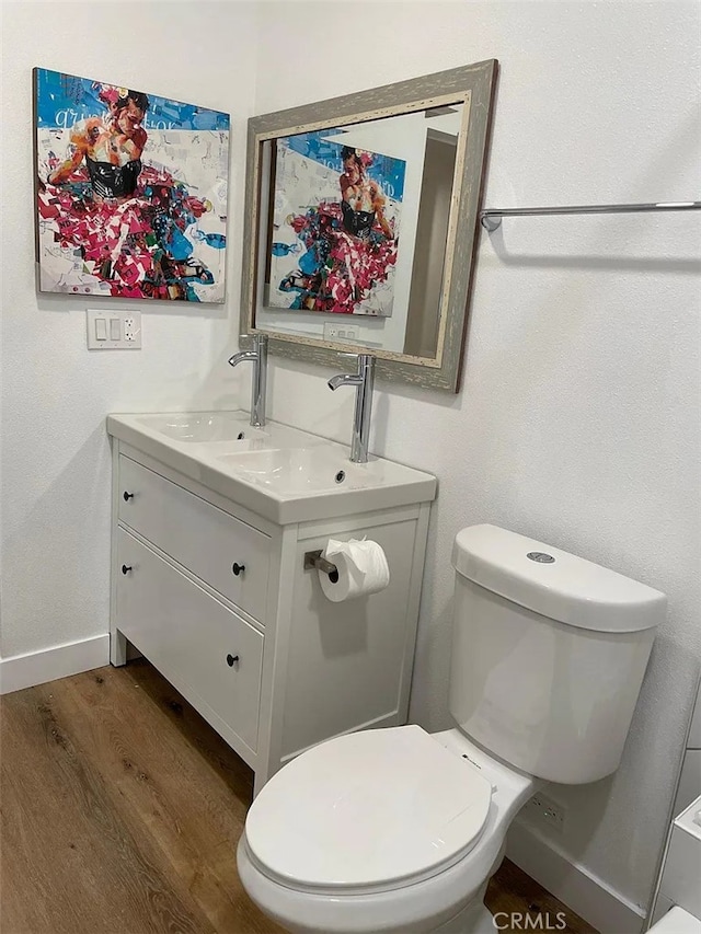 bathroom featuring baseboards, toilet, wood finished floors, and vanity