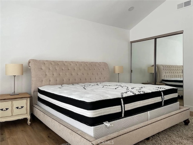 bedroom featuring vaulted ceiling, wood finished floors, visible vents, and a closet