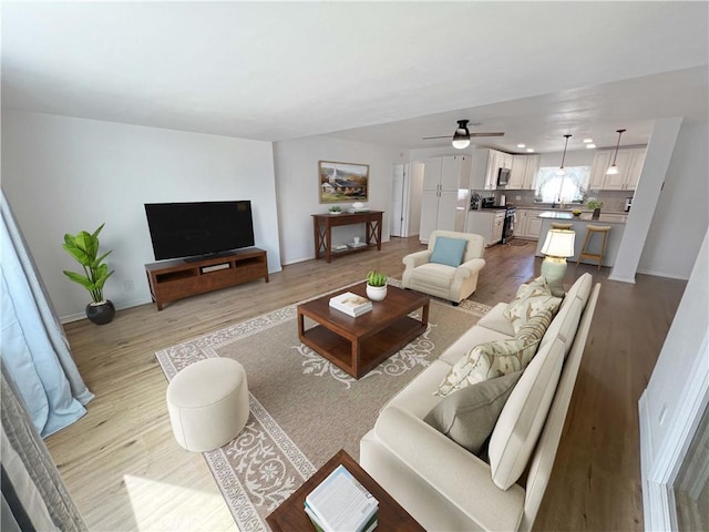 living room with baseboards, light wood-style floors, and a ceiling fan