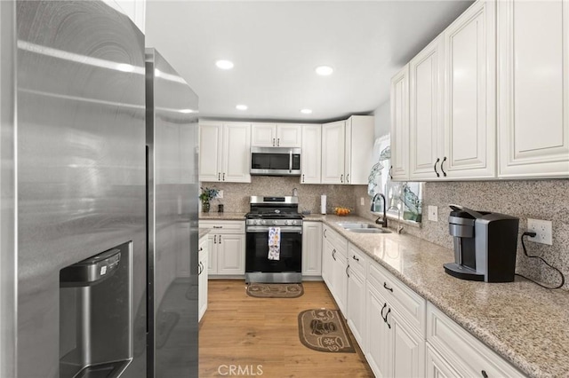 kitchen featuring light wood finished floors, tasteful backsplash, appliances with stainless steel finishes, white cabinets, and a sink