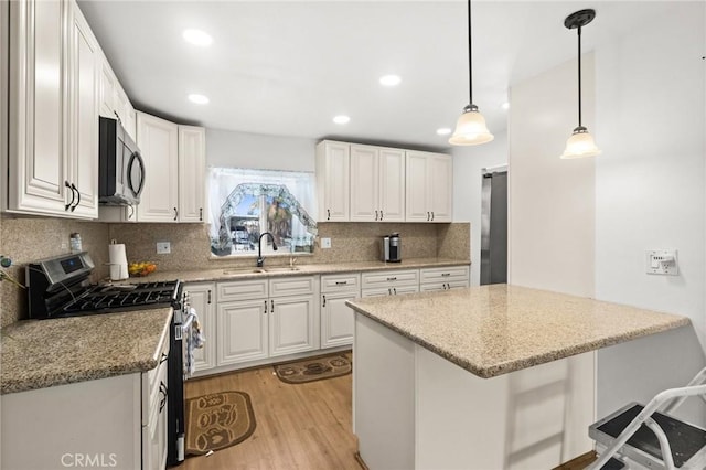 kitchen with white cabinets, appliances with stainless steel finishes, light wood-style floors, and a sink