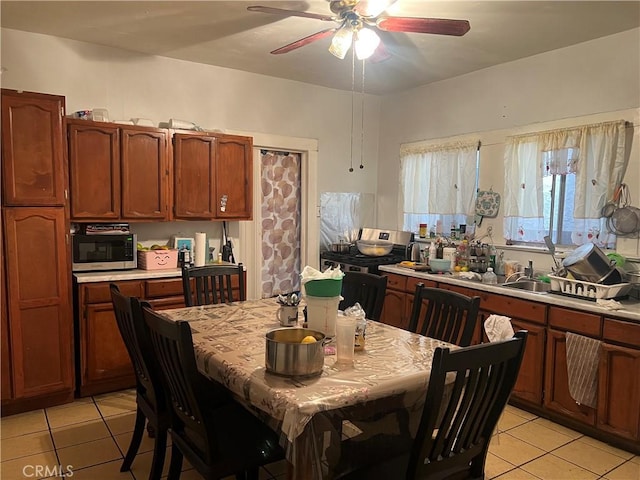 kitchen with light tile patterned floors, brown cabinetry, ceiling fan, stainless steel microwave, and light countertops