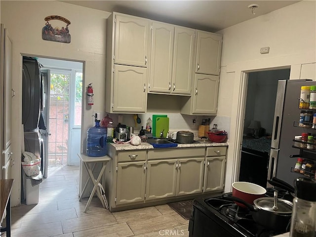 kitchen with white cabinets, stacked washer and clothes dryer, freestanding refrigerator, light countertops, and gas stove