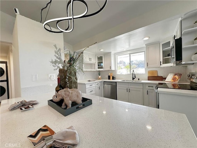 kitchen with light stone counters, decorative backsplash, stainless steel dishwasher, a sink, and stacked washing maching and dryer