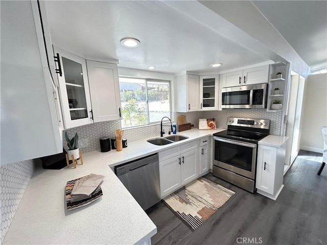 kitchen with dark wood-style flooring, stainless steel appliances, light countertops, white cabinetry, and a sink