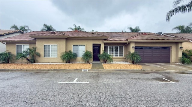 view of front facade with stucco siding, a garage, driveway, and a tiled roof