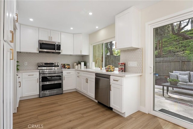 kitchen featuring stainless steel appliances, white cabinets, a sink, and light wood finished floors