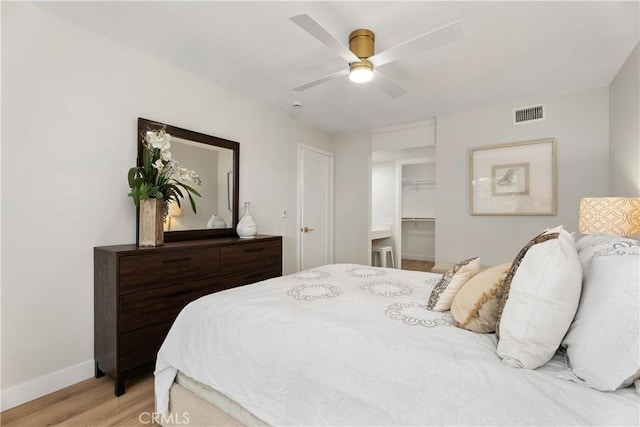 bedroom featuring ceiling fan, light wood-style flooring, visible vents, baseboards, and a walk in closet