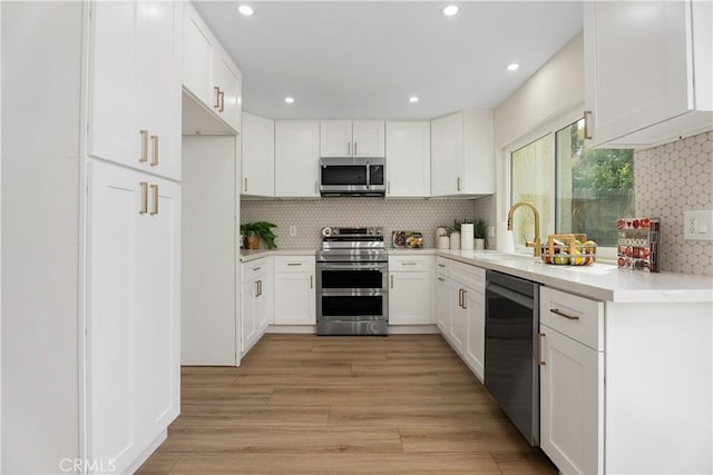 kitchen featuring a sink, white cabinets, appliances with stainless steel finishes, light wood-type flooring, and tasteful backsplash