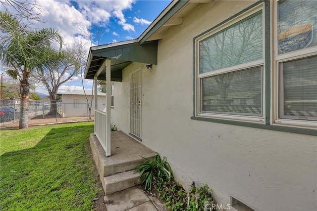 view of side of property with fence, a lawn, and stucco siding