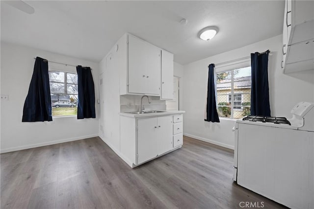 kitchen with wood finished floors, white gas range, light countertops, white cabinetry, and a sink