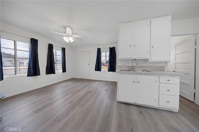 kitchen with light countertops, light wood-style floors, white cabinets, a sink, and baseboards