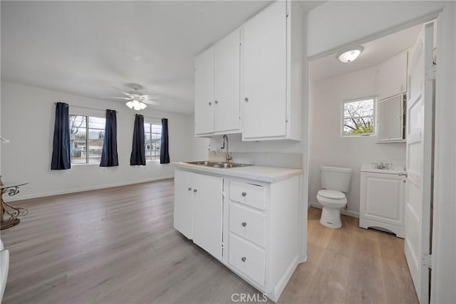 kitchen with light wood finished floors, baseboards, light countertops, white cabinetry, and a sink