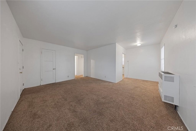 empty room with carpet floors, heating unit, and radiator