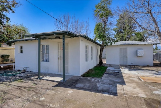 view of side of property featuring stucco siding, a patio area, fence, and an outdoor structure