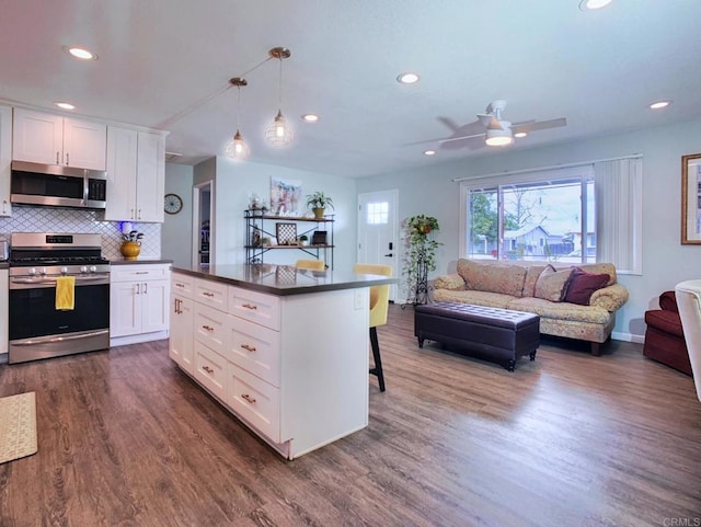 kitchen with stainless steel appliances, dark countertops, open floor plan, and white cabinetry