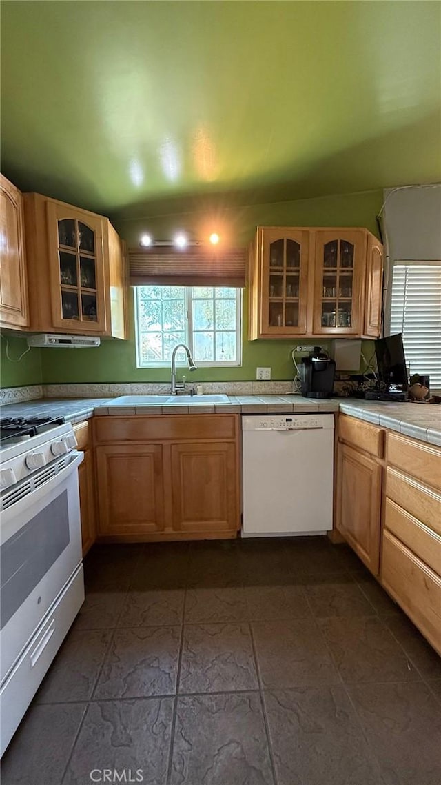 kitchen with glass insert cabinets, white appliances, a sink, and tile countertops