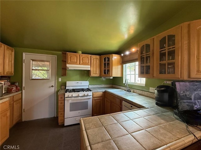 kitchen with tile countertops, glass insert cabinets, white range with gas cooktop, a sink, and under cabinet range hood