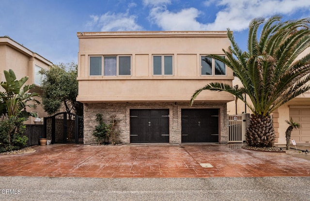 view of front facade with an attached garage, a gate, driveway, and stucco siding