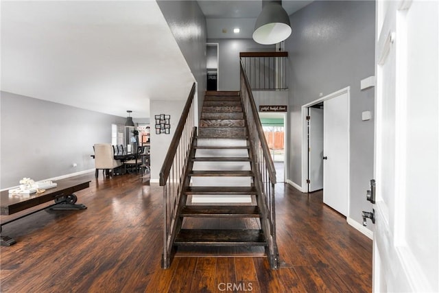 stairway with wood finished floors, a towering ceiling, and baseboards