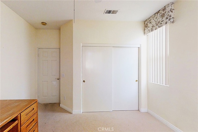 unfurnished bedroom featuring light carpet, baseboards, visible vents, and a closet