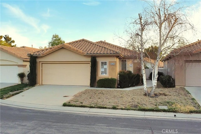 view of front of property featuring an attached garage, a tile roof, concrete driveway, and stucco siding