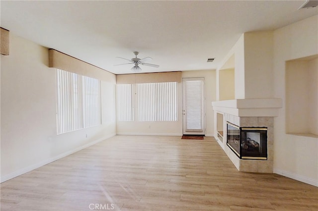 unfurnished living room with ceiling fan, light wood finished floors, a tiled fireplace, and visible vents