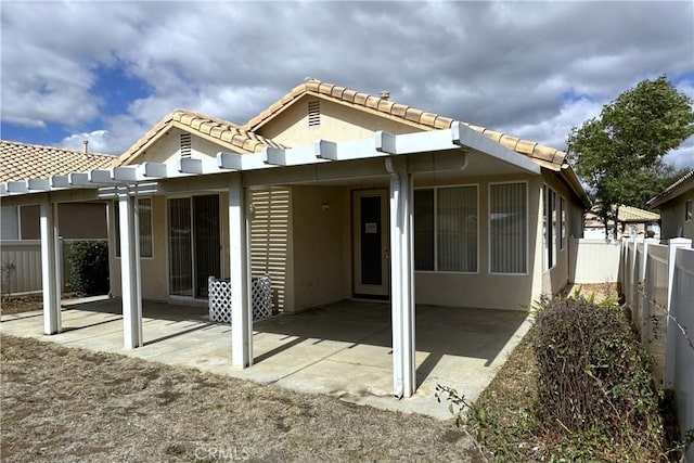 rear view of house featuring a patio, a tile roof, fence, and stucco siding