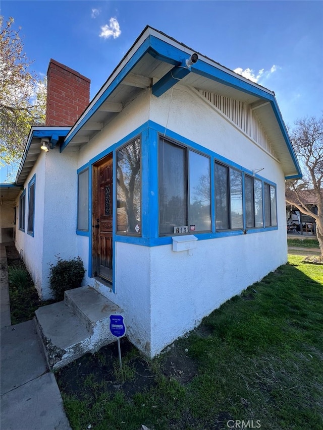 view of side of property featuring a yard, a chimney, and stucco siding