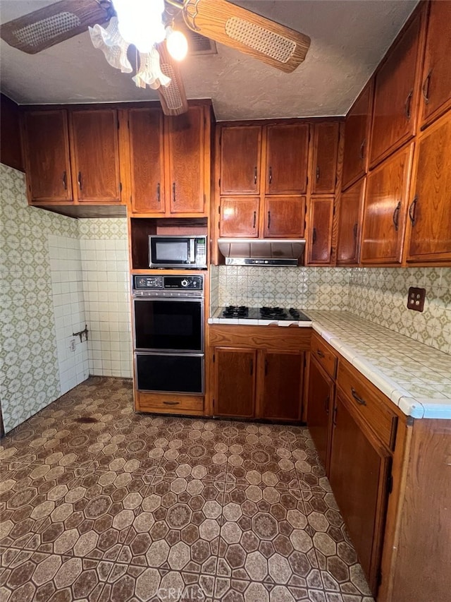 kitchen with decorative backsplash, a ceiling fan, under cabinet range hood, black appliances, and a warming drawer