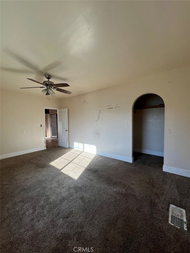 carpeted empty room with arched walkways, a ceiling fan, and baseboards