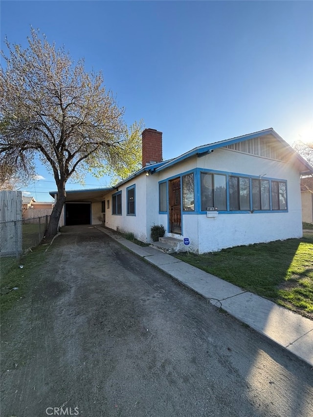 view of front of house with a chimney, stucco siding, a front yard, fence, and driveway