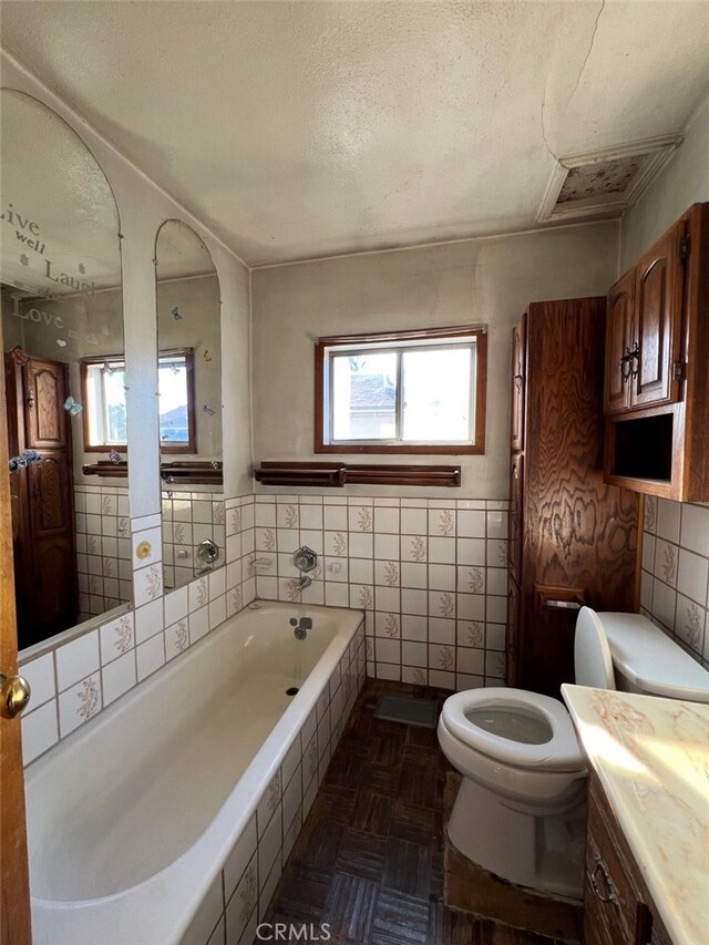 full bathroom with a relaxing tiled tub, a wealth of natural light, a textured ceiling, and toilet