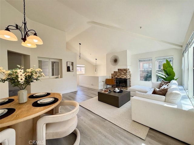 living area featuring a chandelier, high vaulted ceiling, a stone fireplace, and wood finished floors