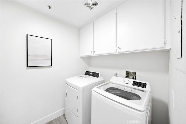 clothes washing area with cabinet space, visible vents, separate washer and dryer, wood finished floors, and baseboards