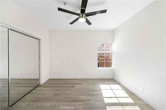 unfurnished bedroom featuring a closet, ceiling fan, baseboards, and wood finished floors