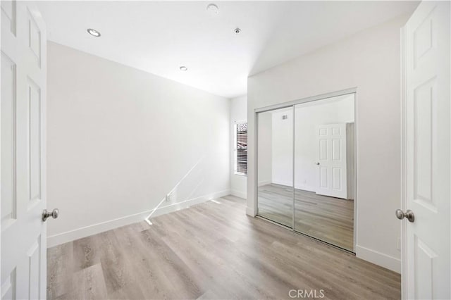 unfurnished bedroom with a closet, recessed lighting, wood finished floors, and baseboards