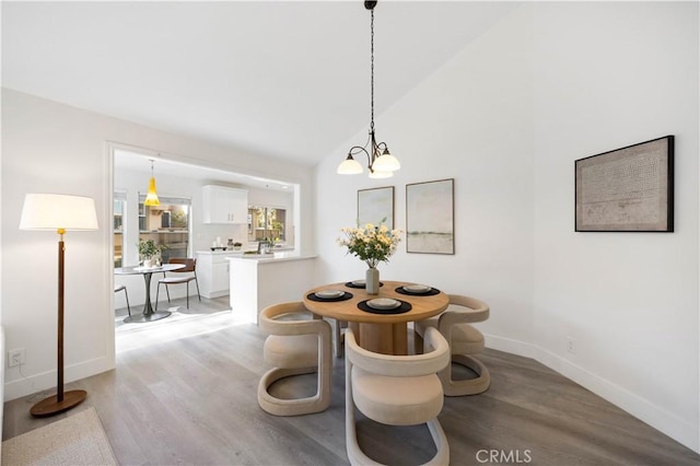 dining area with a chandelier, light wood-type flooring, vaulted ceiling, and baseboards