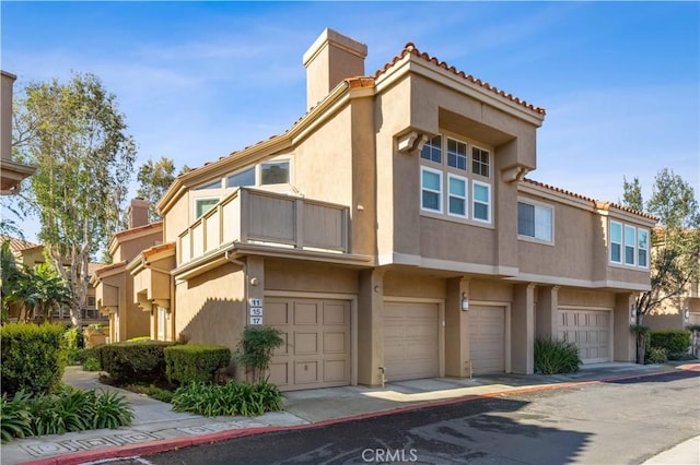 exterior space featuring a chimney, an attached garage, a balcony, and stucco siding