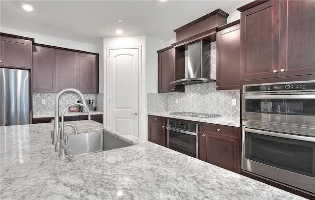 kitchen featuring a sink, stainless steel appliances, light stone counters, and wall chimney exhaust hood