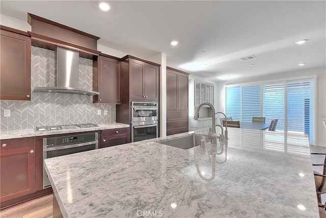 kitchen featuring visible vents, decorative backsplash, stainless steel appliances, wall chimney exhaust hood, and a sink