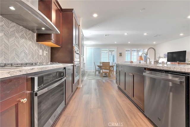 kitchen with recessed lighting, decorative backsplash, light wood-style floors, appliances with stainless steel finishes, and wall chimney range hood