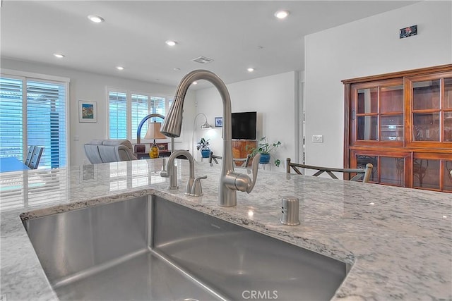 kitchen with visible vents, light stone countertops, open floor plan, recessed lighting, and a sink