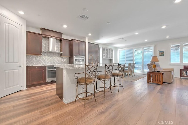 kitchen with visible vents, a kitchen bar, light wood-style flooring, appliances with stainless steel finishes, and wall chimney exhaust hood