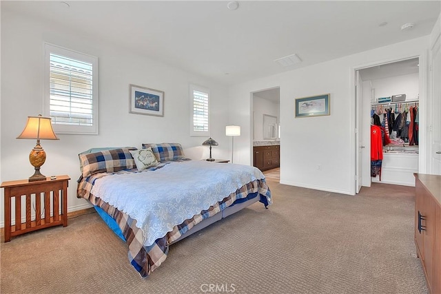 bedroom featuring a spacious closet, baseboards, light colored carpet, a closet, and ensuite bath