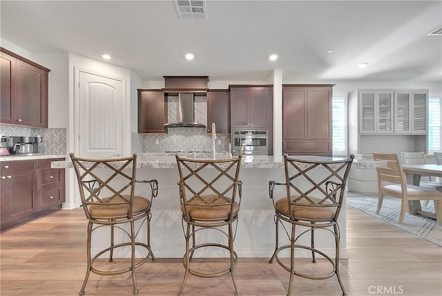 kitchen with a breakfast bar, wall chimney exhaust hood, visible vents, and light wood finished floors