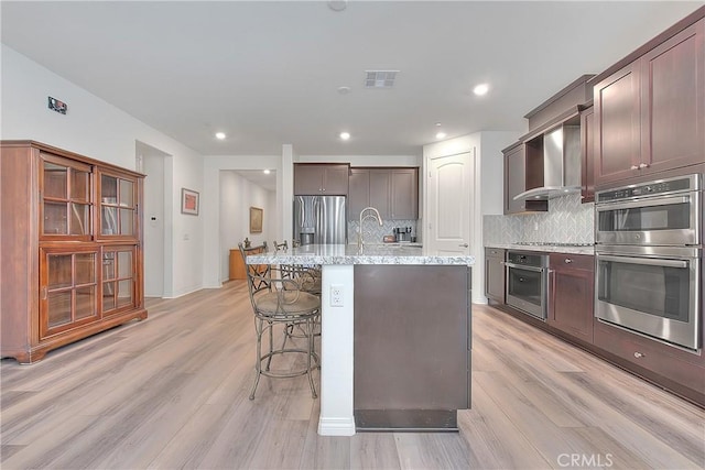 kitchen featuring visible vents, backsplash, appliances with stainless steel finishes, a kitchen breakfast bar, and wall chimney exhaust hood