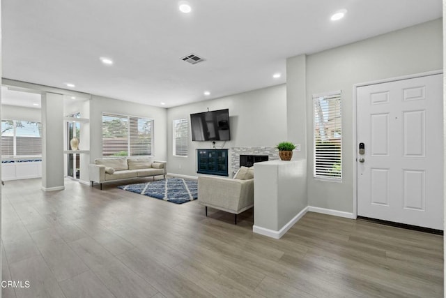 living room with a glass covered fireplace, wood finished floors, visible vents, and recessed lighting