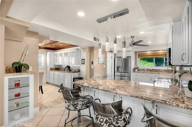 kitchen with light tile patterned floors, a peninsula, white cabinetry, appliances with stainless steel finishes, and light stone countertops