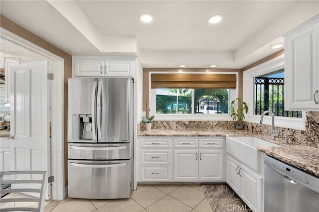 kitchen with light tile patterned floors, appliances with stainless steel finishes, white cabinetry, a sink, and light stone countertops